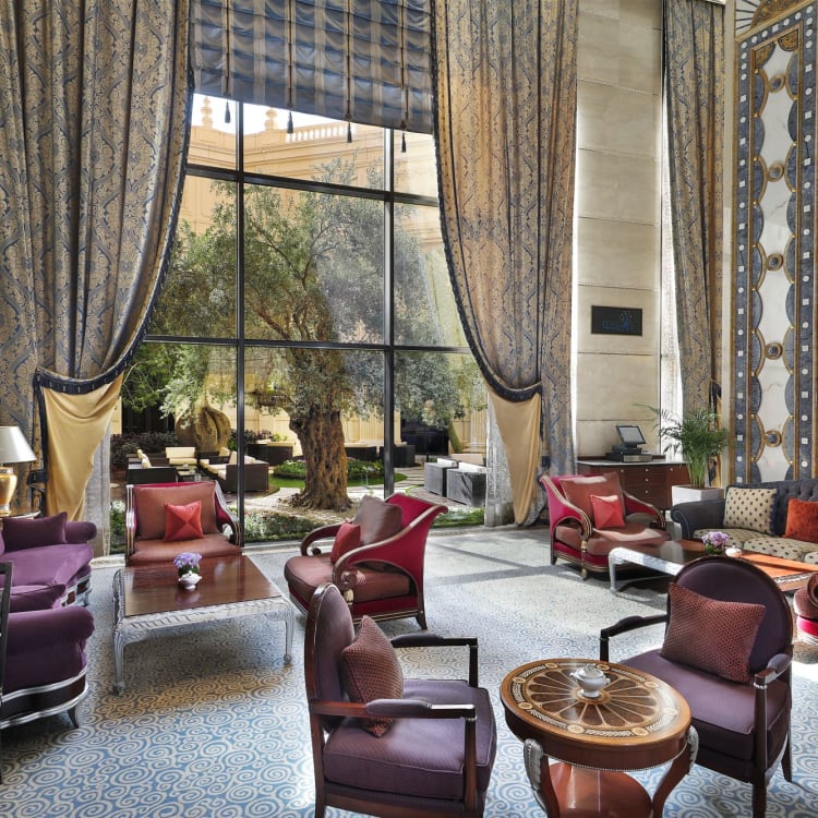 A lounge of a hotel with various seating areas in front of a window facing a garden