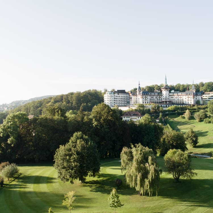 Eine landschaftlich schöne Aussicht auf das Dolder Grand Hotel mit üppigen grünen Gärten und sanften Hügeln im Hintergrund.