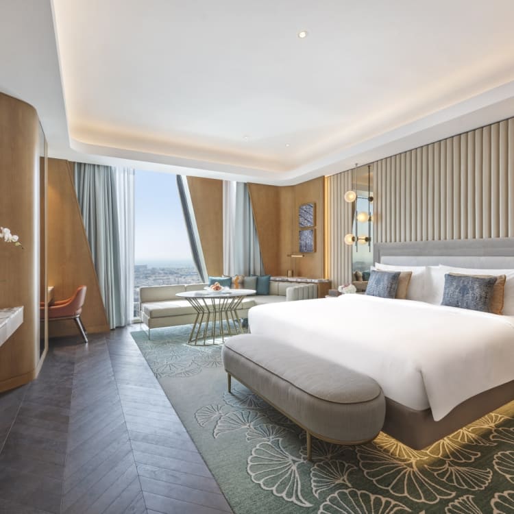 Ein luxuriöses Hotelzimmer mit großem Bett, Sitzbereich in der Nähe der Fenster und eleganter Dekoration.