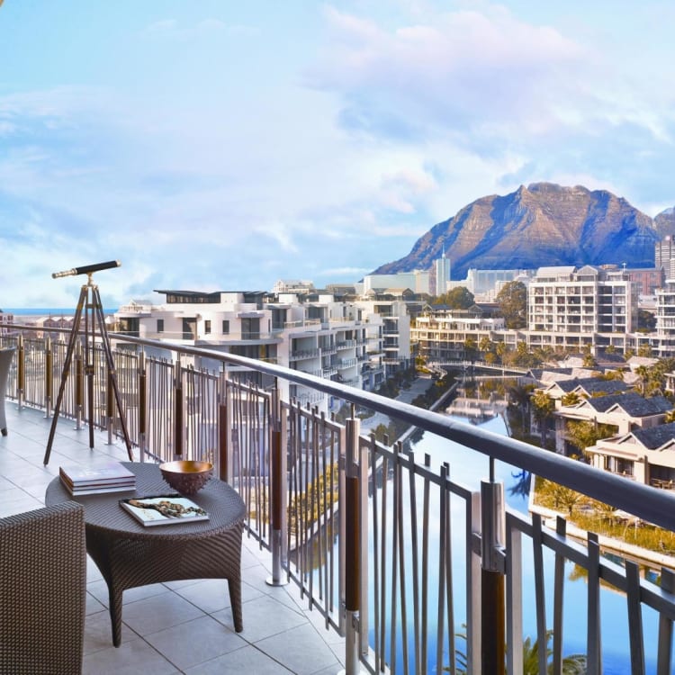 A luxurious suite balcony overlooking Cape Town with a view of Table Mountain, furnished with outdoor chairs, a table, and a telescope.