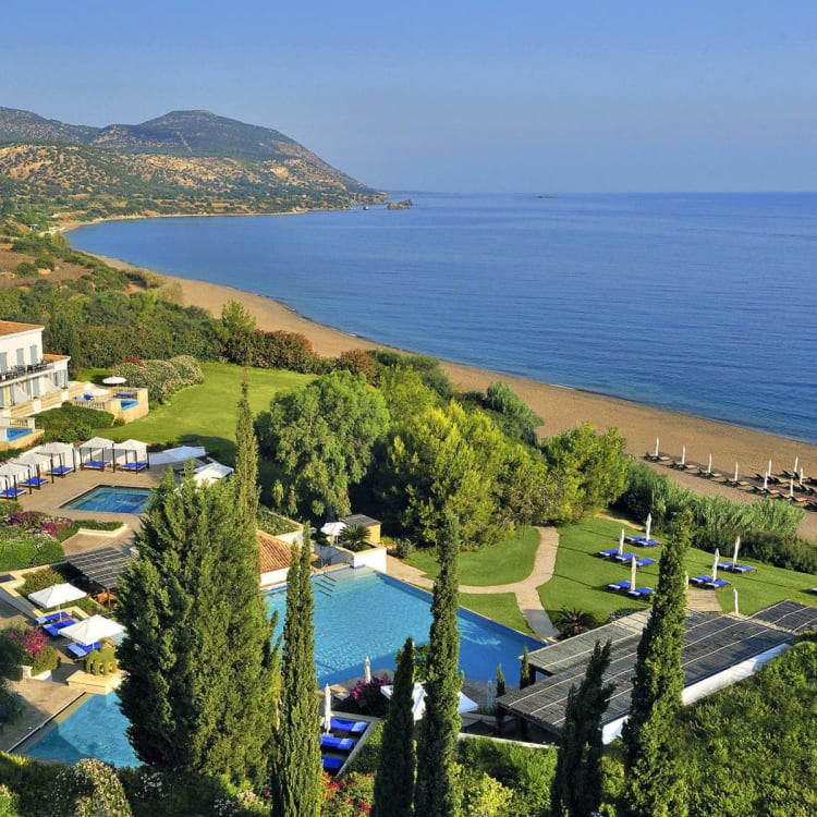 Aerial view of Anassa Zypern Resort featuring swimming pools, lush greenery, a sandy beach, and the sea in the background.