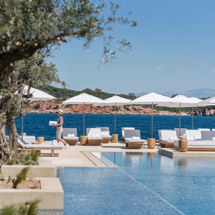 Luxurious outdoor pool area at Four Seasons Astir Palace Hotel Athens with white sunbeds, umbrellas, and a view of the sea in Greece.