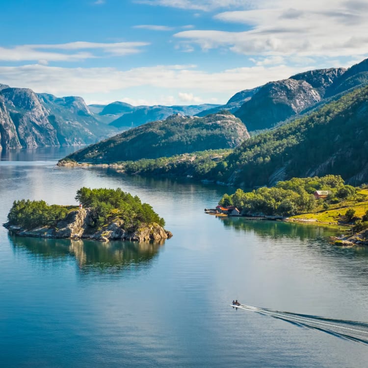 Calm fjord landscape surrounded by steep, rocky mountains with green vegetation and small islands under a partly cloudy sky, a boat leaving a wake in the water.