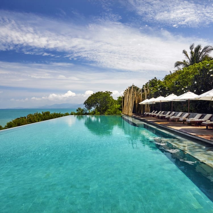 Infinity pool overlooking the ocean with lounge chairs and umbrellas on a tropical island.