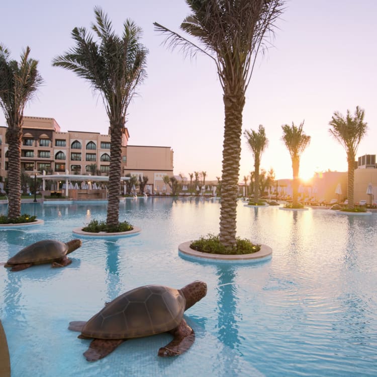 Luxury hotel pool with palm trees and turtle sculptures during sunset in Abu Dhabi.