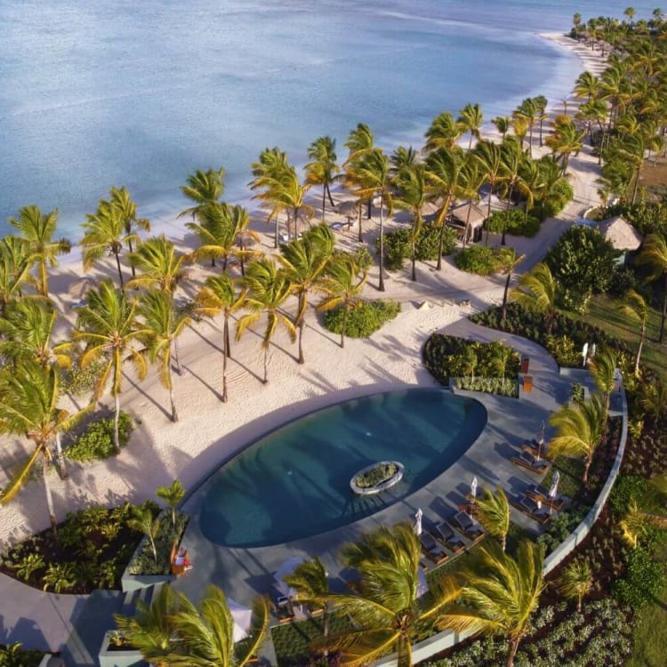 Luftaufnahme eines luxuriösen Pools, umgeben von Palmen an einem tropischen Resort am Strand.