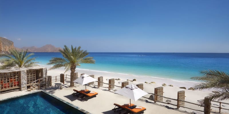 Ein luxuriöses Strandresort mit einem Swimmingpool, weißem Sandstrand, Palmen und Sonnenliegen mit Sonnenschirmen mit Blick auf den Ozean.