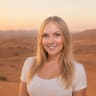 A smiling young woman with long blonde hair standing in a desert landscape at sunset.