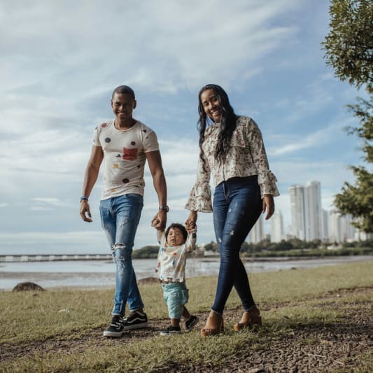 Two parents walking hand-in-hand with toddler in park.