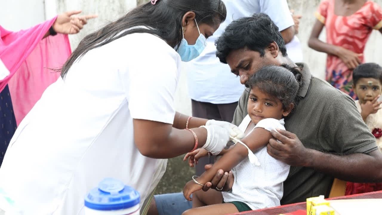 Child sitting in father's lap and receiving vaccine