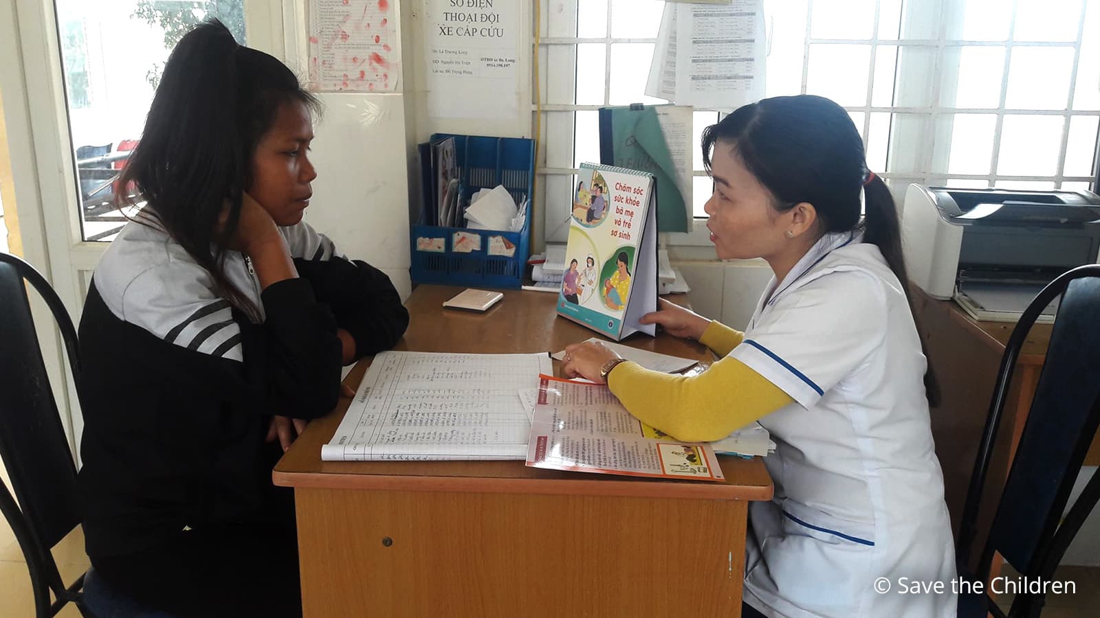 Physician talking with young woman sitting accross her desk. 