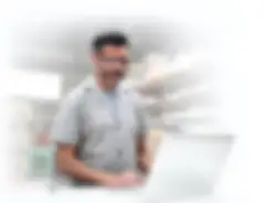 man in grey shirt wearing glasses standing in front of a computer