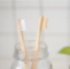 Two toothbrushes with wooden handles in a glass jar and a white tile wall in the background