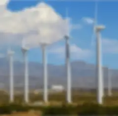 A row of five modern, white wind turbines with mountains in the background