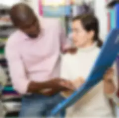 A man offers customer support to a woman who is looking at a blue binder folder in an office supply store