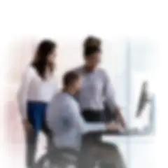 office setting man in wheelchair and two women standing all viewing a computer screen