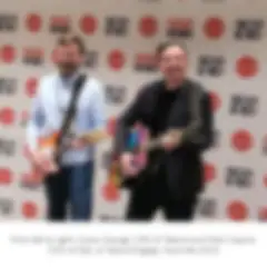 Talend CRO Casey George and Qlik CEO Mike Capone stand smiling while holding guitars  in front of a backdrop with the Talend logo and the phrase together we rock