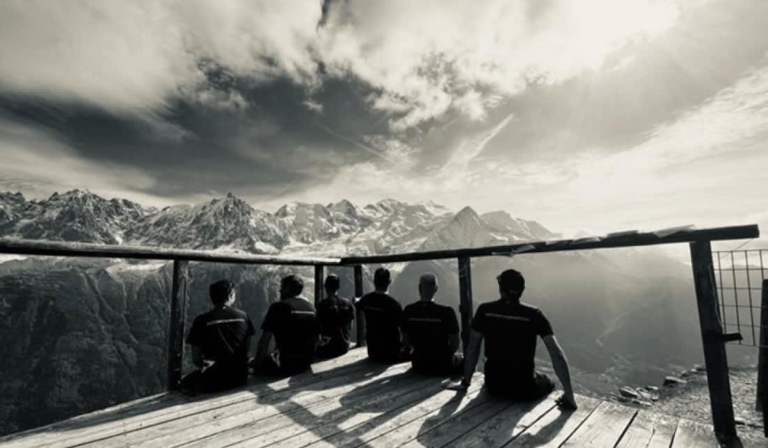 Photo of six people sitting on a wooden platform overlooking a mountain view