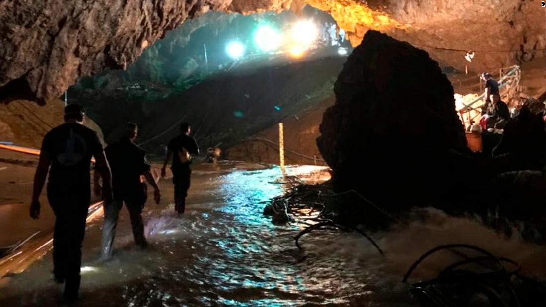 Image of three people carrying flashlights walking out of cavern through a stream of water