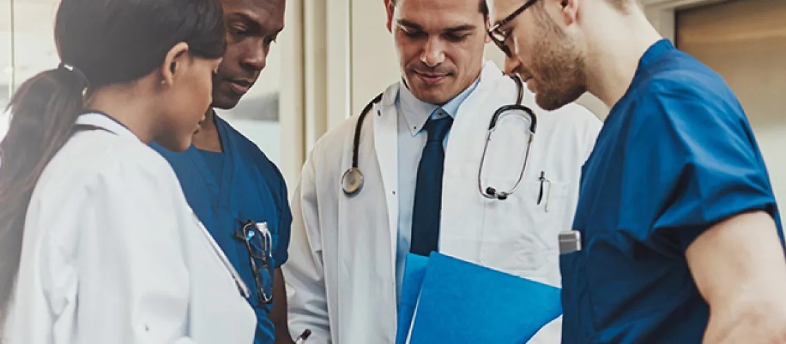 A group of four medical professionals, including two doctors and two nurses, are gathered together, discussing a file in a hospital setting.