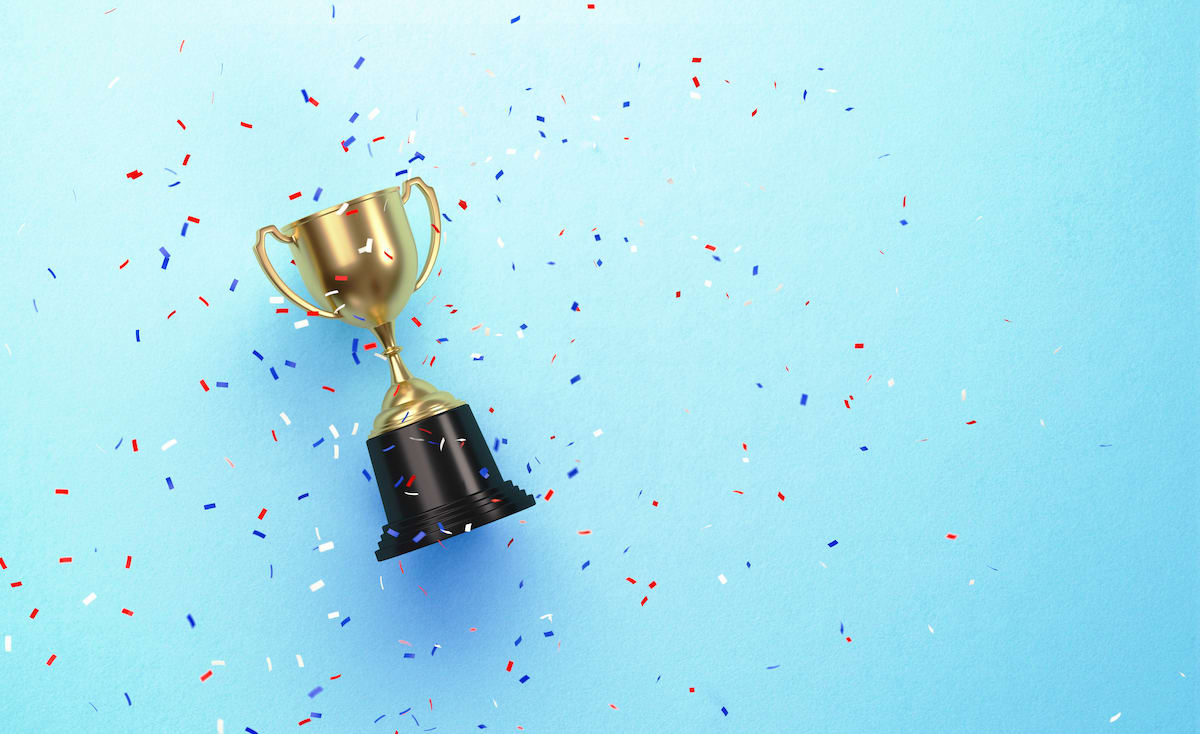 Photo of a gold-cup trophy laying on a light blue surface with colorful confetti sprinkled all around it