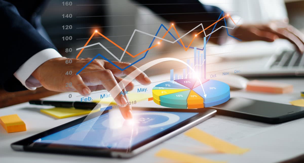 Close-up photo of a man's hand working with a chart on a tablet overlayed with graphics of a pie chart and line graphs