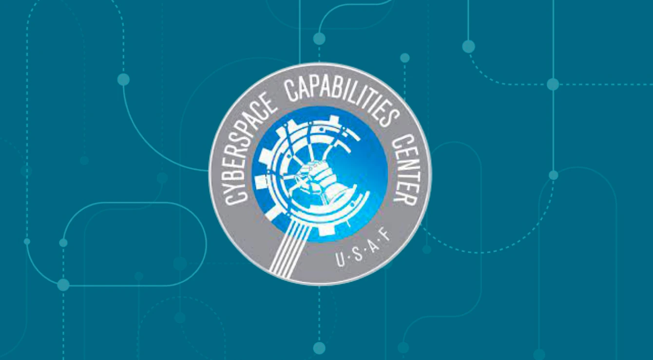 The Cyberspace Capabilities Center emblem of the U.S. Air Force, featuring a circular design with a blue and white graphic in the center and text encircling it on a teal background with node patterns.