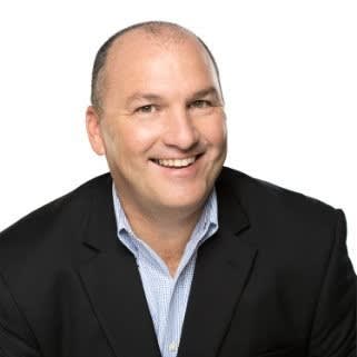 Headshot of blog author Dan Potter. He has short hair, wearing a black suit jacket over a light blue checkered shirt, smiling at the camera.