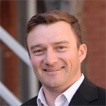 Headshot of blog author Nick Magnuson. He has short brown hair and is wearing a black suit jacket and a white shirt, smiling at the camera.