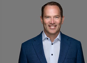 Drew Clarke, General Manager, Data Business Unit wearing a blue suit and white shirt stands against a gray background, smiling at the camera.