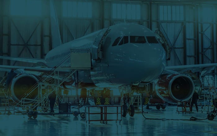 A large commercial airplane is parked inside an aircraft hangar with maintenance equipment and personnel working around it.