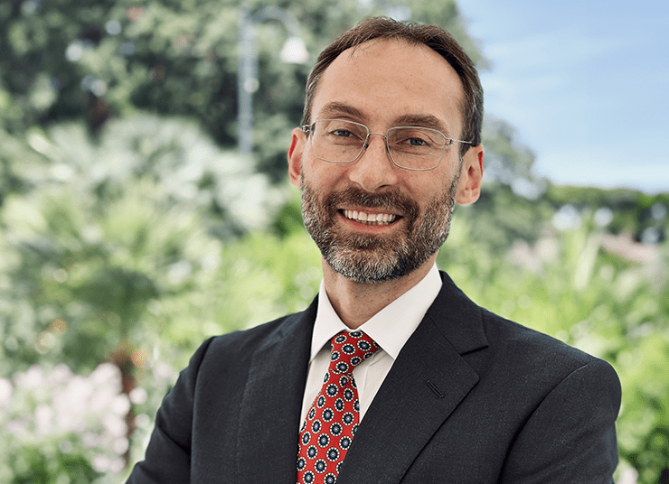 Headshot of Qlik AI Council member, Micahel Bronstein. He is wearing a suit and patterned red tie, smiling and standing outdoors with a background of greenery.