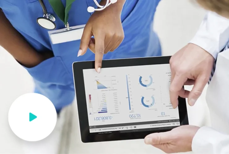 Two medical professionals view and discuss charts and graphs on a tablet. One person points at the screen while the other holds the device. A stethoscope and ID badge are visible.