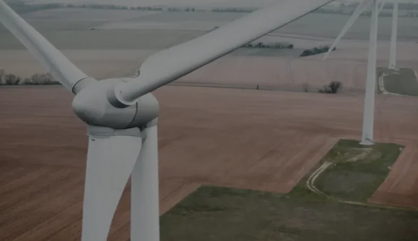 Close-up view of a wind turbine with large white blades set against a backdrop of expansive rural fields.