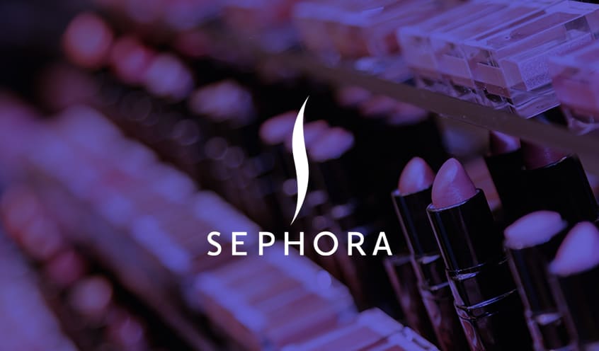 Sephora company logo overlayed over an a close-up image of a row of lipsticks in a display