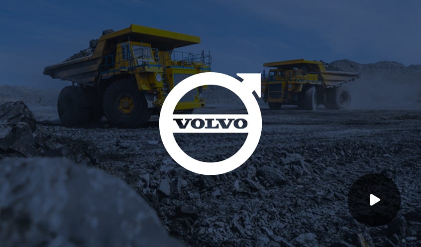 Volvo company logo overlayed on an image of construction trucks in a gravel lot