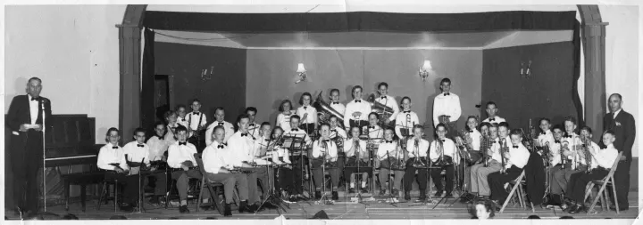(School?) Band on stage at the Idlehour Hall circa 1950 Mr. Jor Morrow \[C.P.R. Policeman} at microphone Back Row (l-r): Barry Bryson, Barry Thompson, Mildred Hunt, Myrna Beeson, John Forester, Jerry Shulson, Margret Gunter, Gloria Staab, ___ Nelson, Ray Herrick, Jim Gunter, Alan Rostad (tall, standing), ? (sitting), Ron Johnson, Don Houston, Robert Halbert, Wayne Aadland, Ernie Penlerick (Bandmaster) Middle Row (l-r): Ken Rostad, Cam Lopston, Marcel Vasseur, Danny Morrow, Jim McNab, Alan Jenson, Jack Green, Kenny Green, Dianne Hesch, Joe Kupkie, Lester Coutts, Gary Houston Front Row (l-r): Bob Lopston, ___ Halbert, David Heming, Bob Arnold, Jack Pearpoint, Darlene Kirkpatrick, Barrett Halderman, ?, Barry Bryson