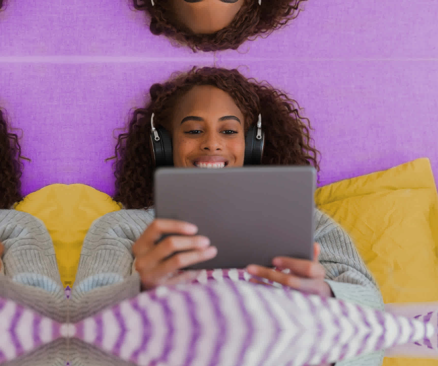 A woman wearing headphones under a blanket watching video on a tablet
