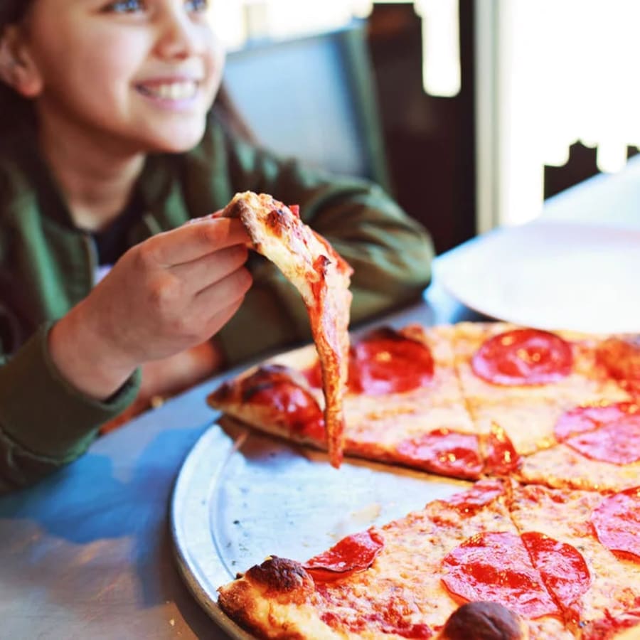 A guest smiling over a pepperoni pizza at Lucy's