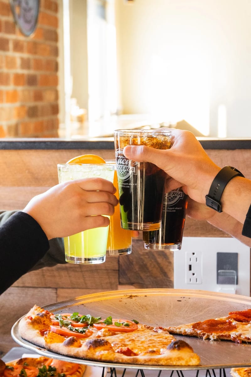 Guests raising Lucy's pint glasses over a pizza