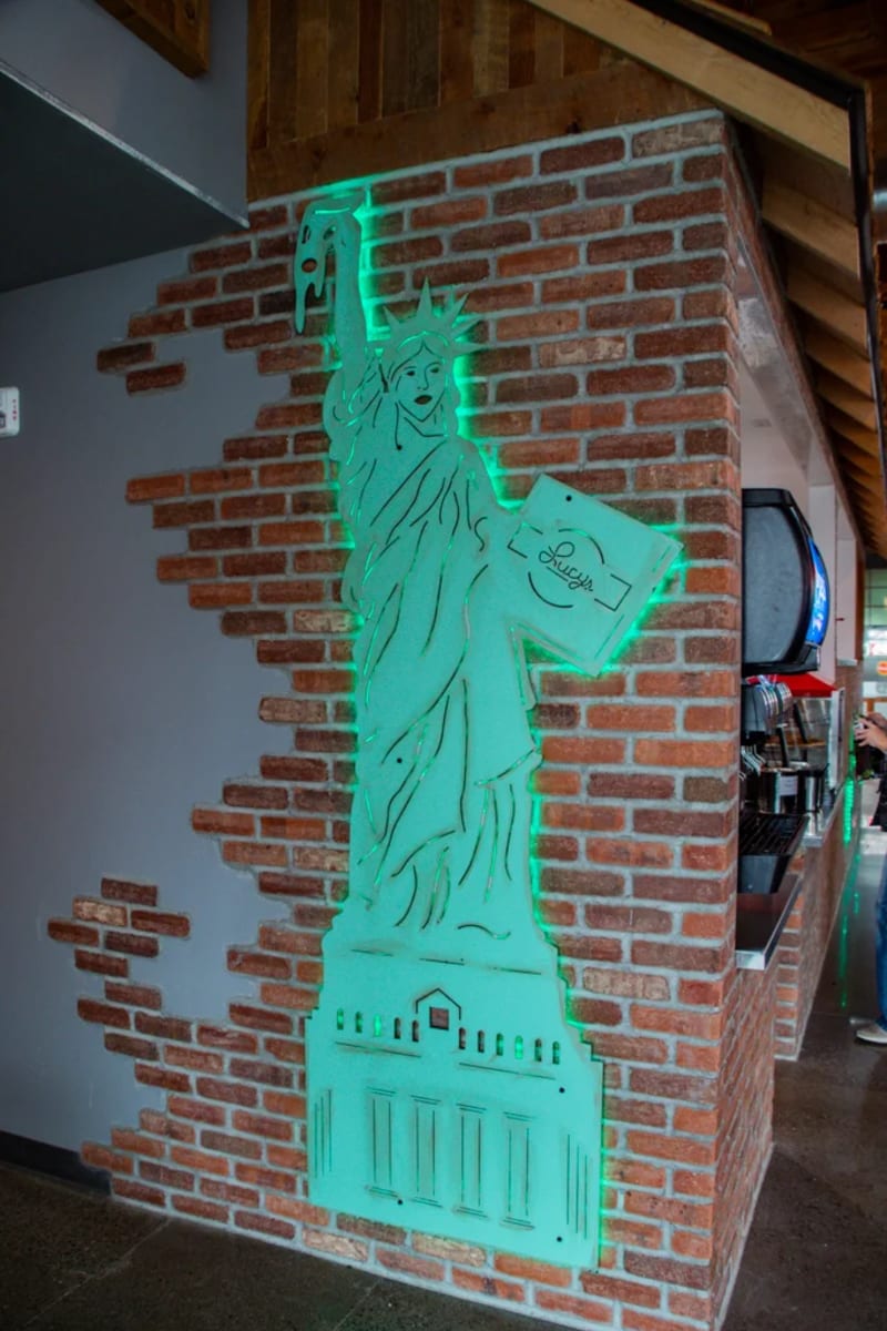 The neon Statue of Liberty holding a pizza box on the brick wall at Lucy's