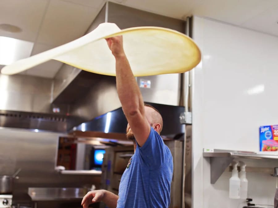 A Lucy's dough master tossing pizza dough in the kitchen