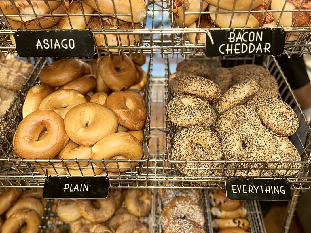 Baskets of asiago, bacon cheddar, plain and everything bagels under chalk labels