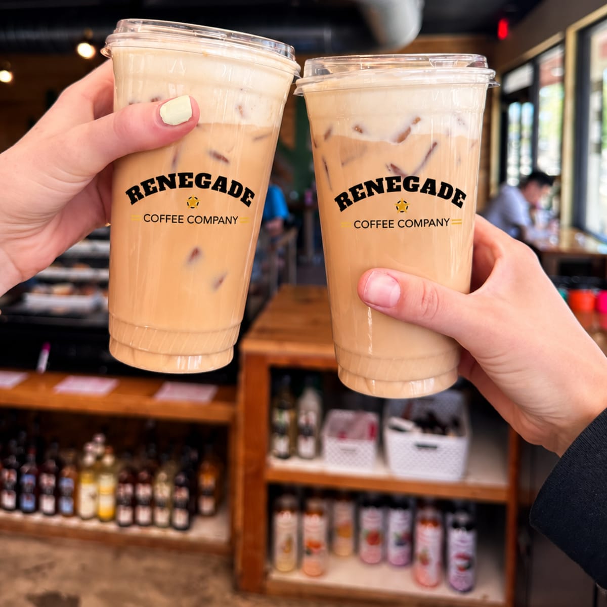 Two hands clinking iced Renegade Coffee drinks together