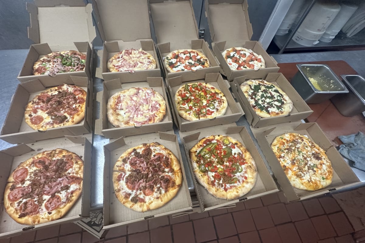A dozen Pizza Kitchen pizzas boxed up for a catering order