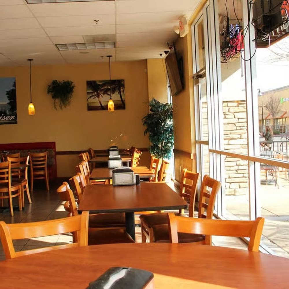 Sunlit dining room at Rancho Steve's Pizza with wooden tables and chairs beside tall front windows