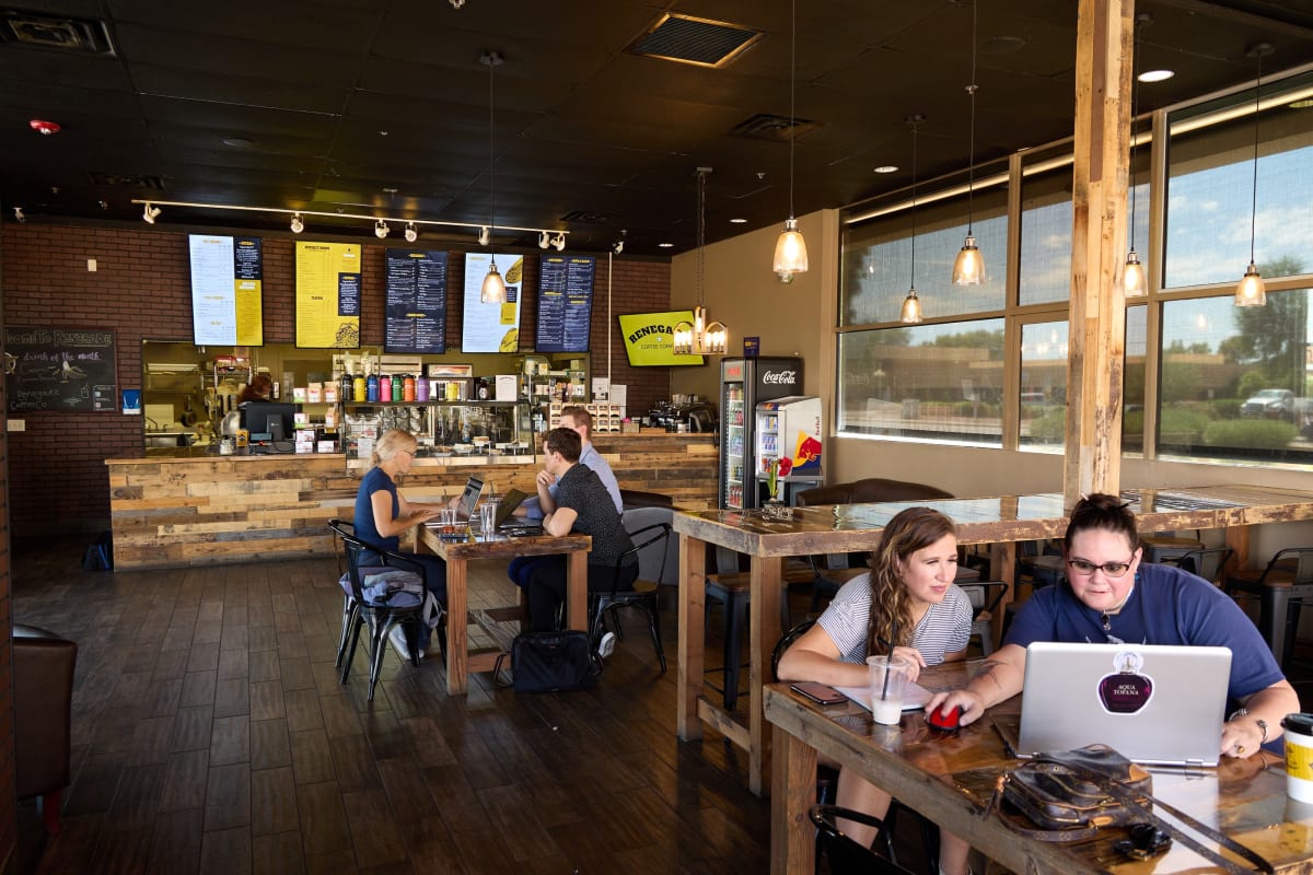 Two guests working on laptops at a long reclaimed-wood table at Renegade Coffee
