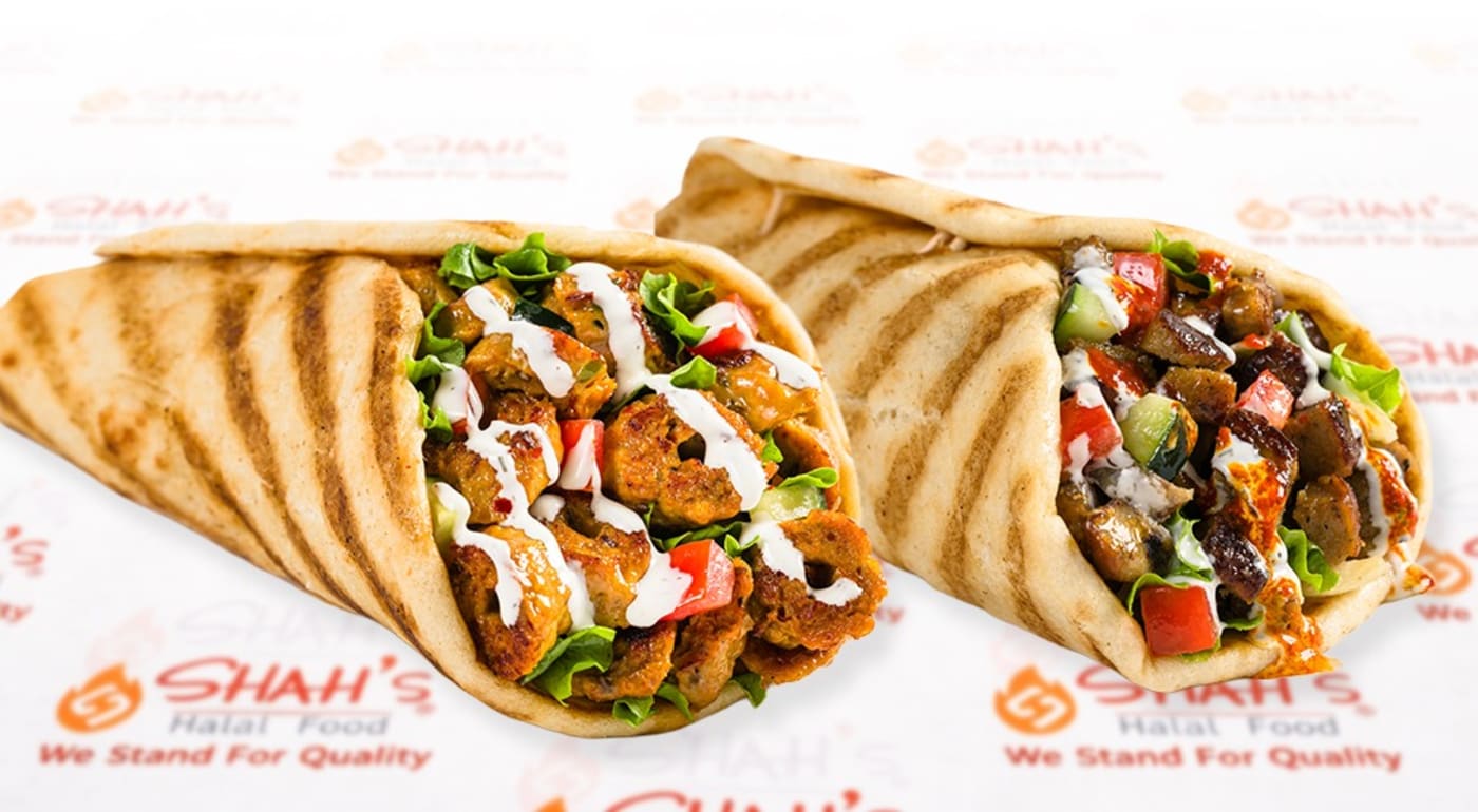Two Shah's gyros on branded wrapper paper, drizzled with white sauce