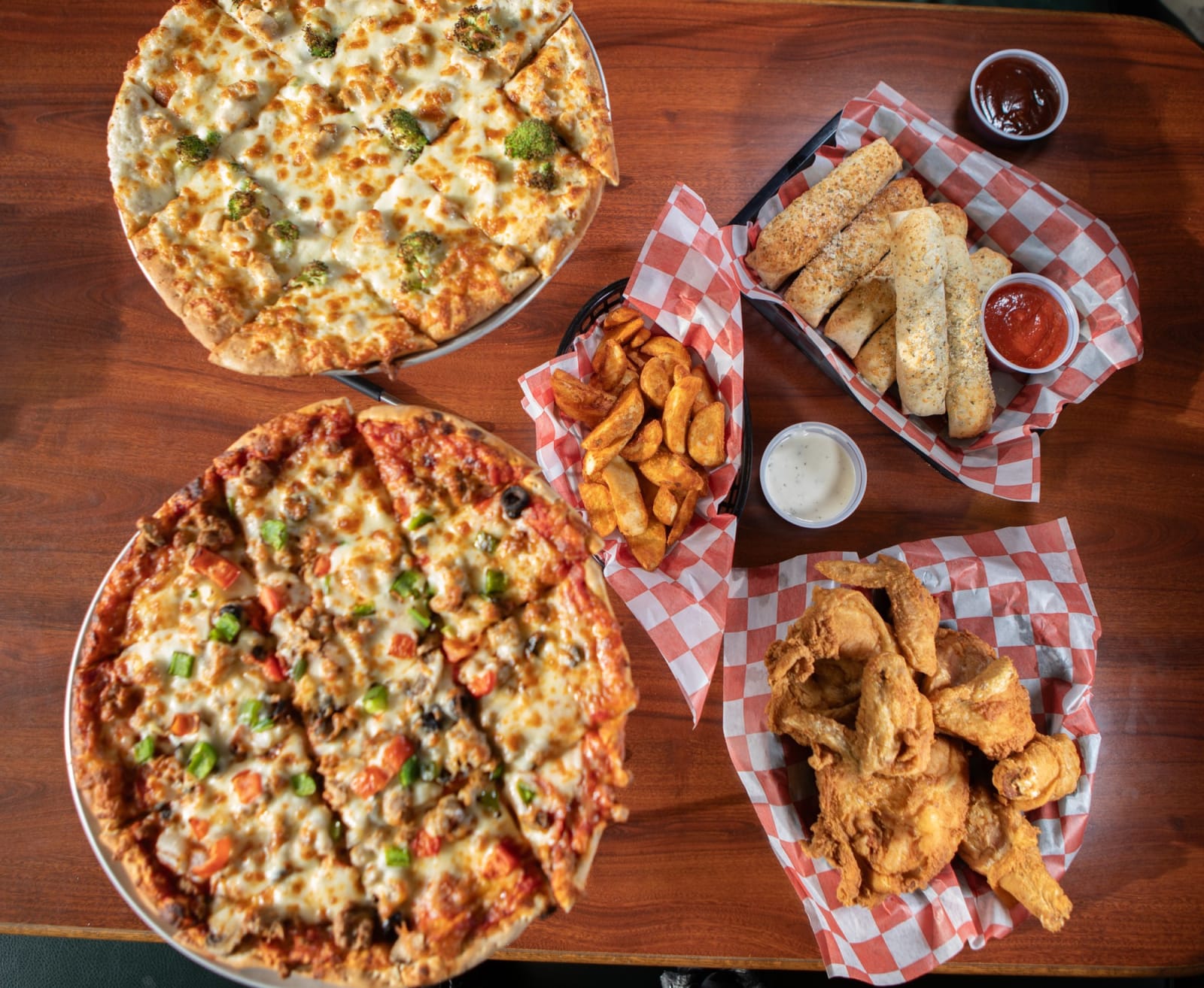 A catering spread of Boss' pizzas, breadsticks, wedges and chicken on a wooden table