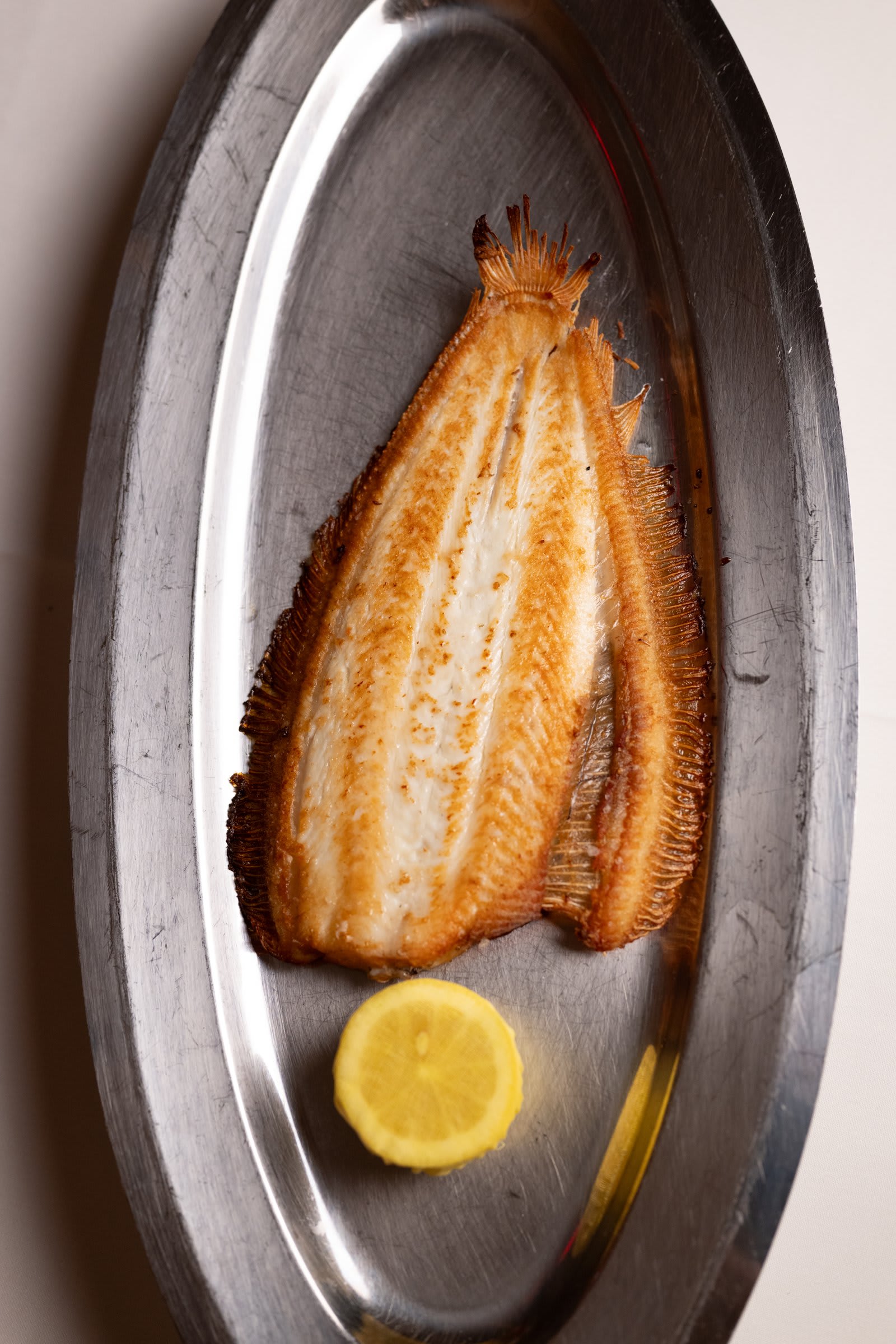A whole butterflied fish on a silver platter with lemon, carried to the table at Castell's